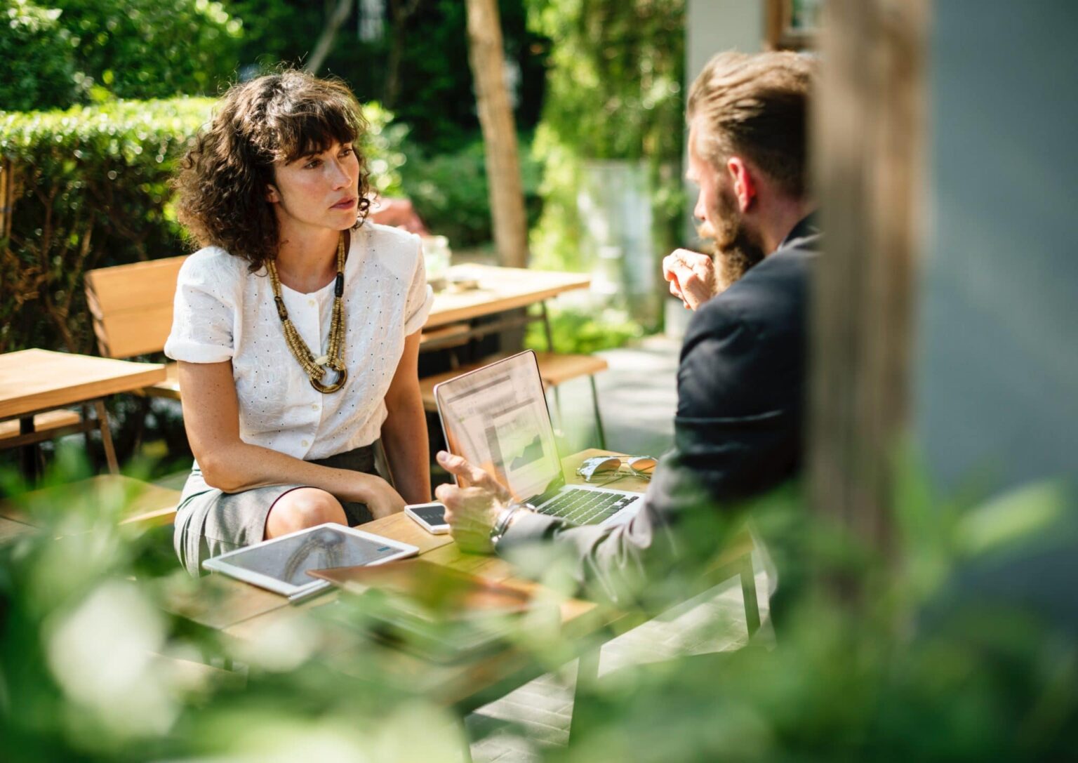 man and woman sitting at a table in a garden having a discussion
