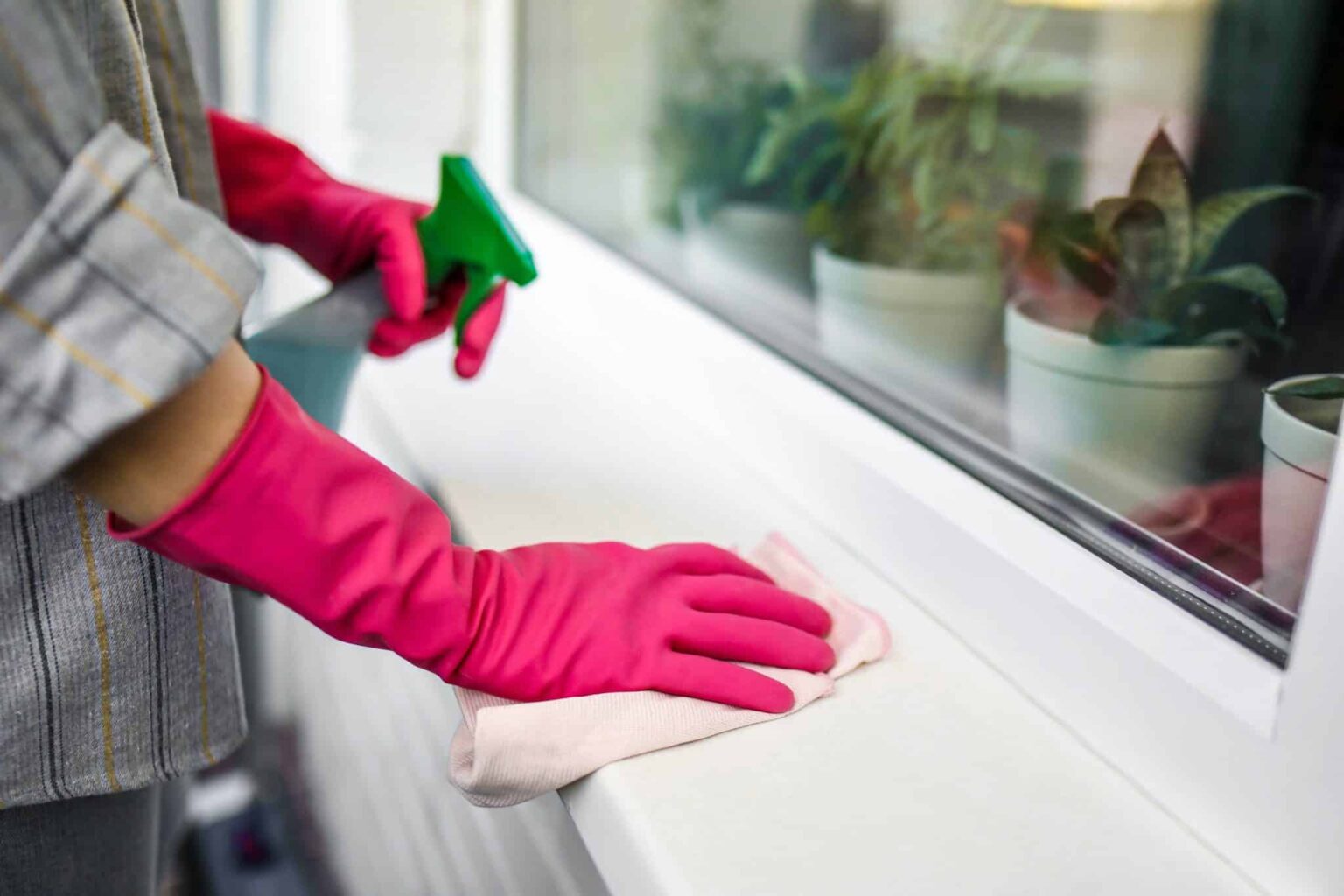 Person wiping off their window sill with spray cleaner.