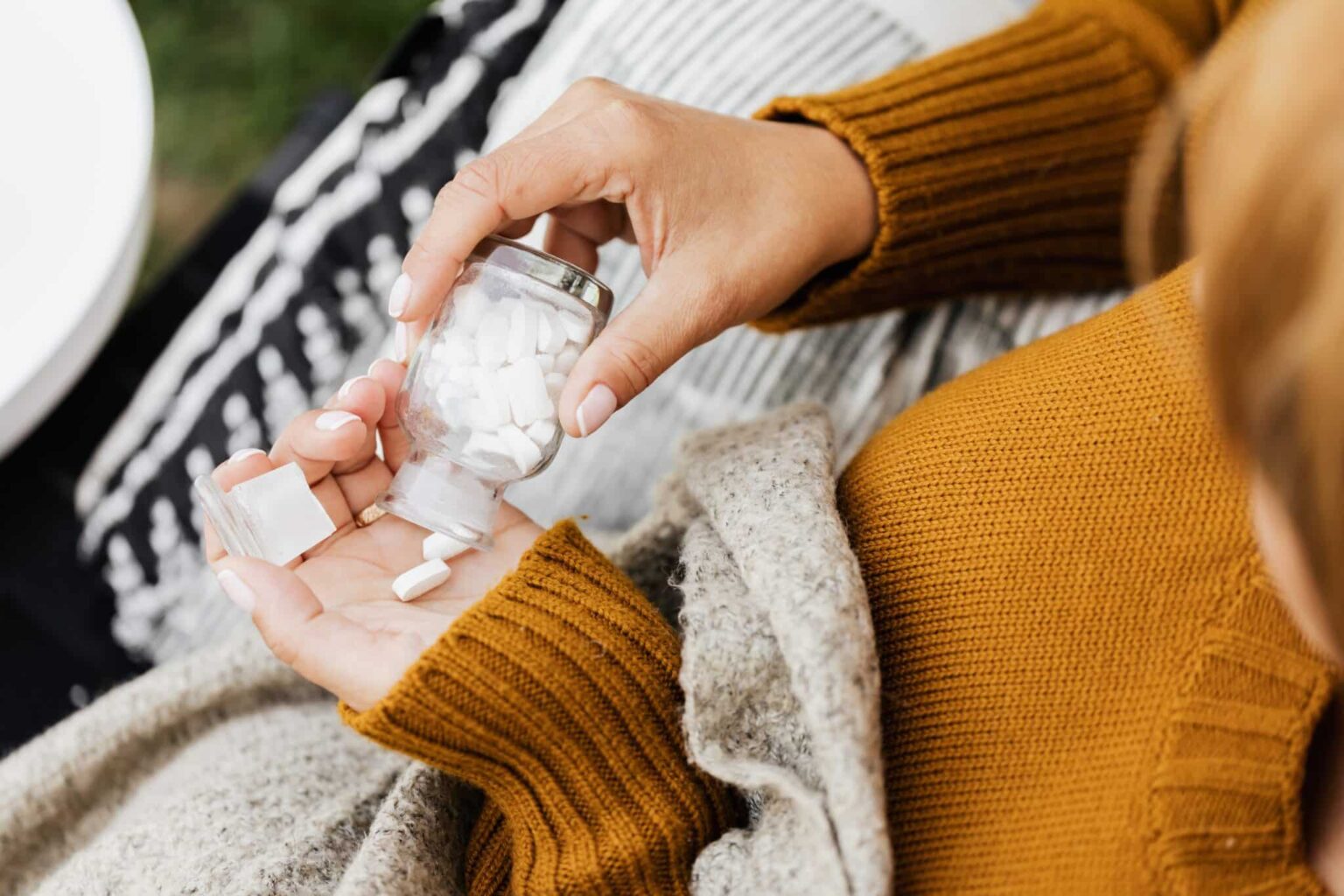 A close-up of a person taking medication from a bottle.