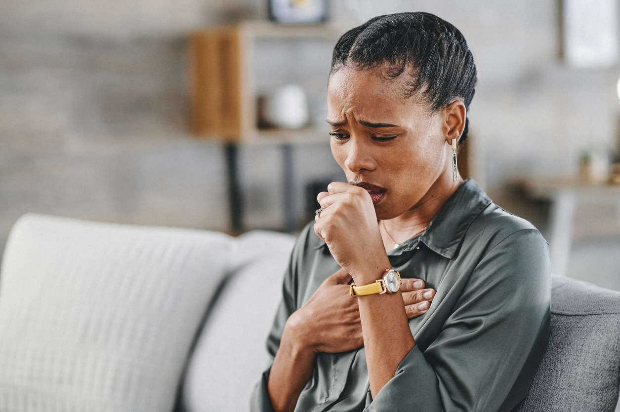 Close-up of woman coughing on sofa at home